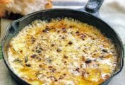 A cast-iron skillet filled with baked fontina cheese, nearby is a hunk of bread
