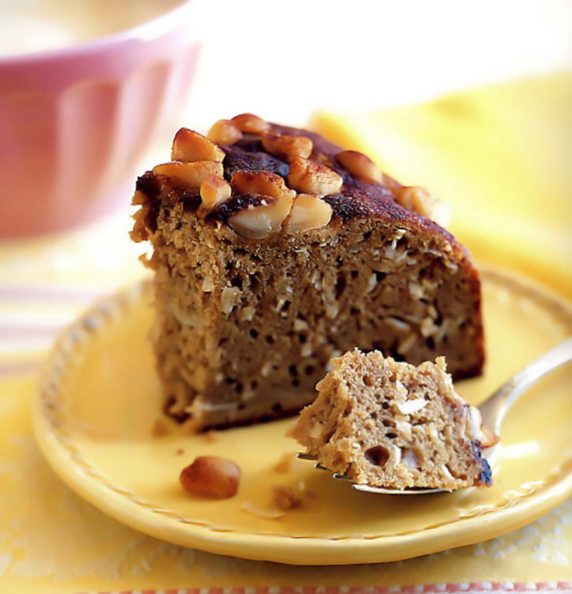 A slice of banana and macadamia nut coffee cake on a yellow plate with a fork holding a bite of it.