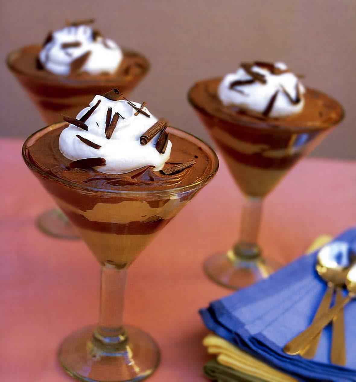 Three martini glasses filled with layers of chocolate brownie mousse, topped with whipped cream and chocolate shavings