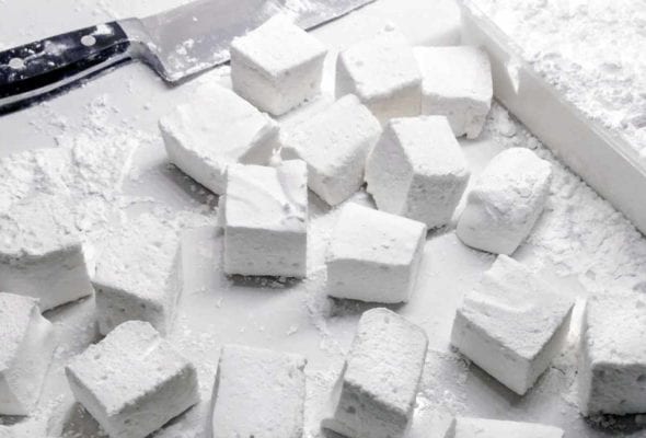 Cubes of homemade marshmallows on a white surface with a chef's knife lying beside.