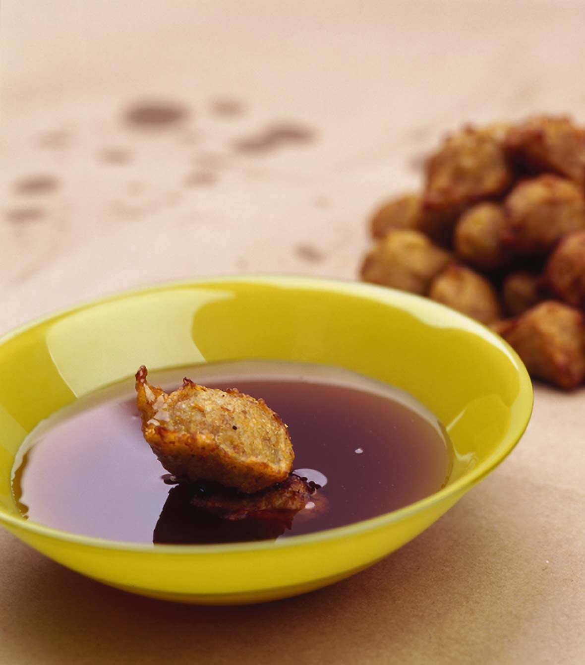 Yellow bowl with a banana fritter and honey, more fritters in the back on brown paper
