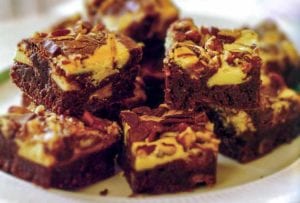 Plate of cream cheese swirl brownies with layers of chocolate, cheese cake, Heath bar, and pecans