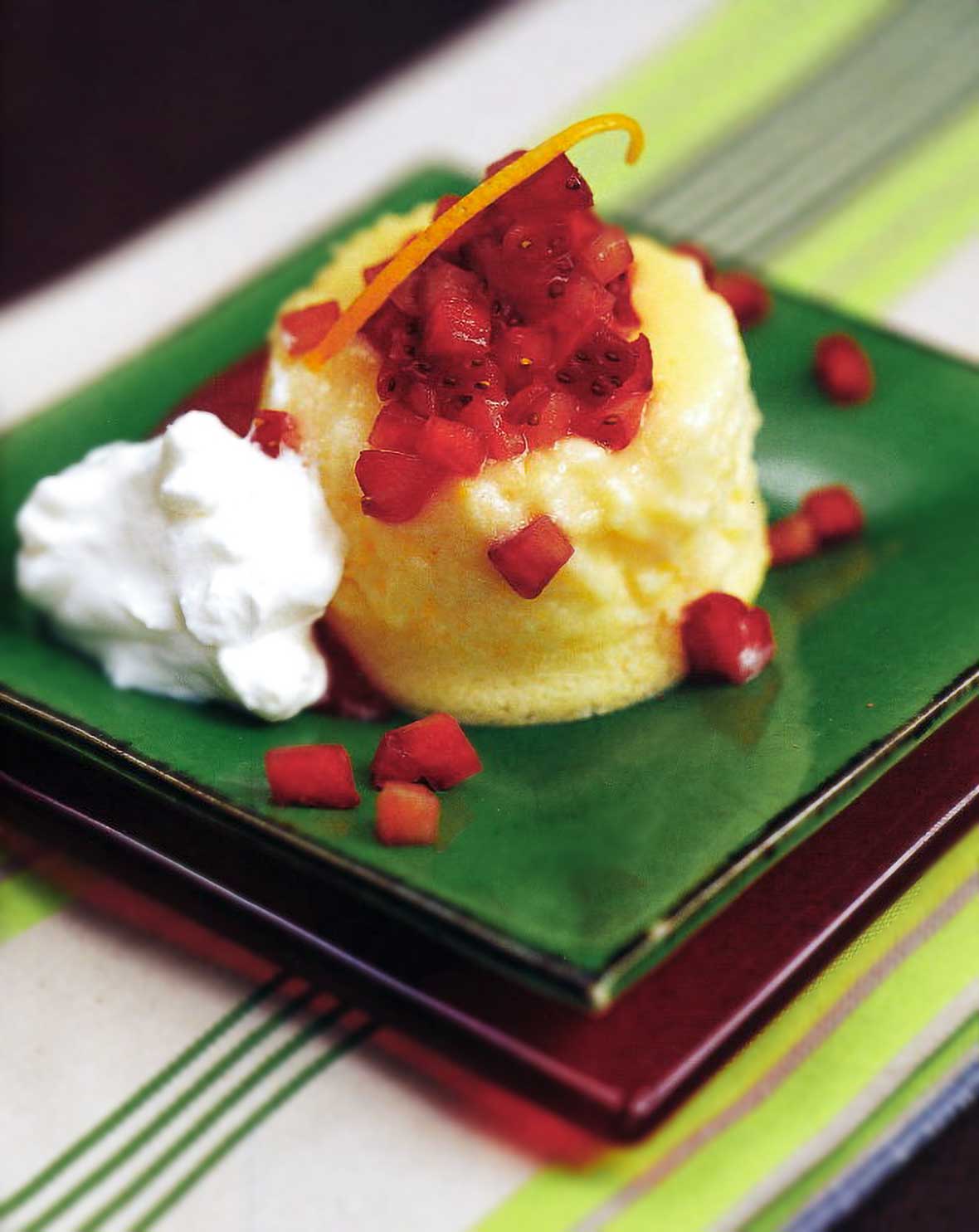 Green square plate with a lemon-buttermilk pudding cake topped with strawberries and orange zest, whipped cream