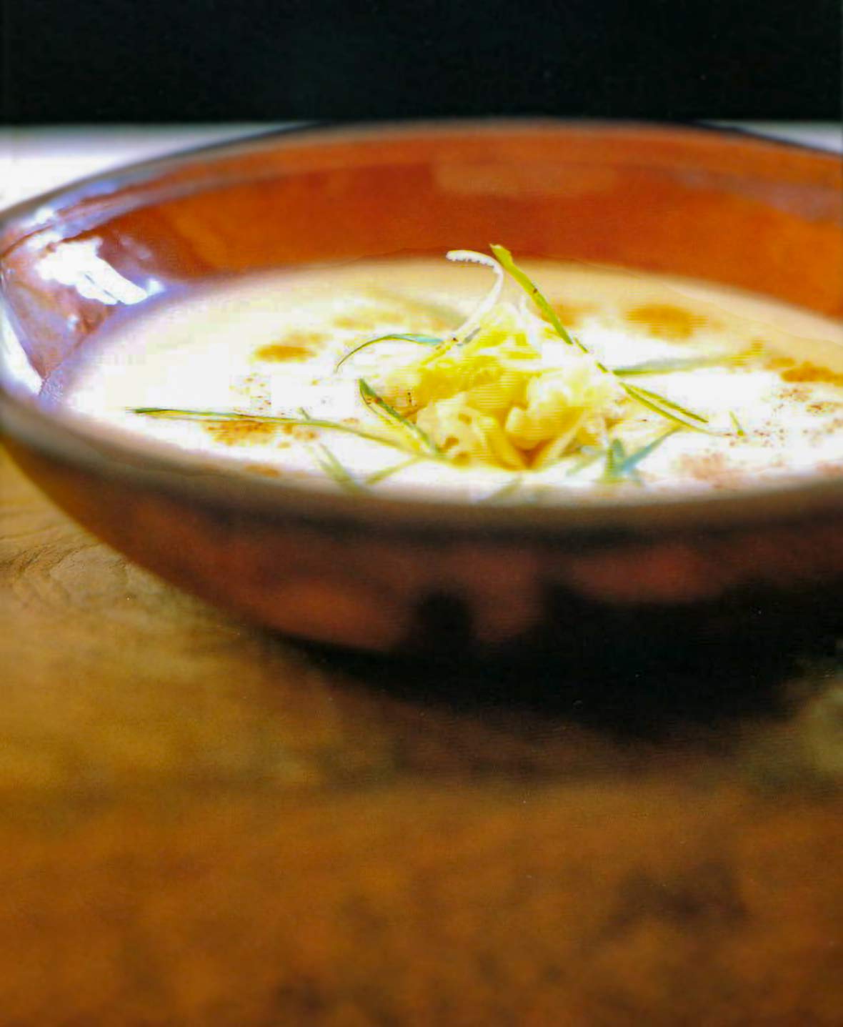 Brown bowl of spicy Swiss potato soup with scallion, Gruyere cheese, and potatoes on top