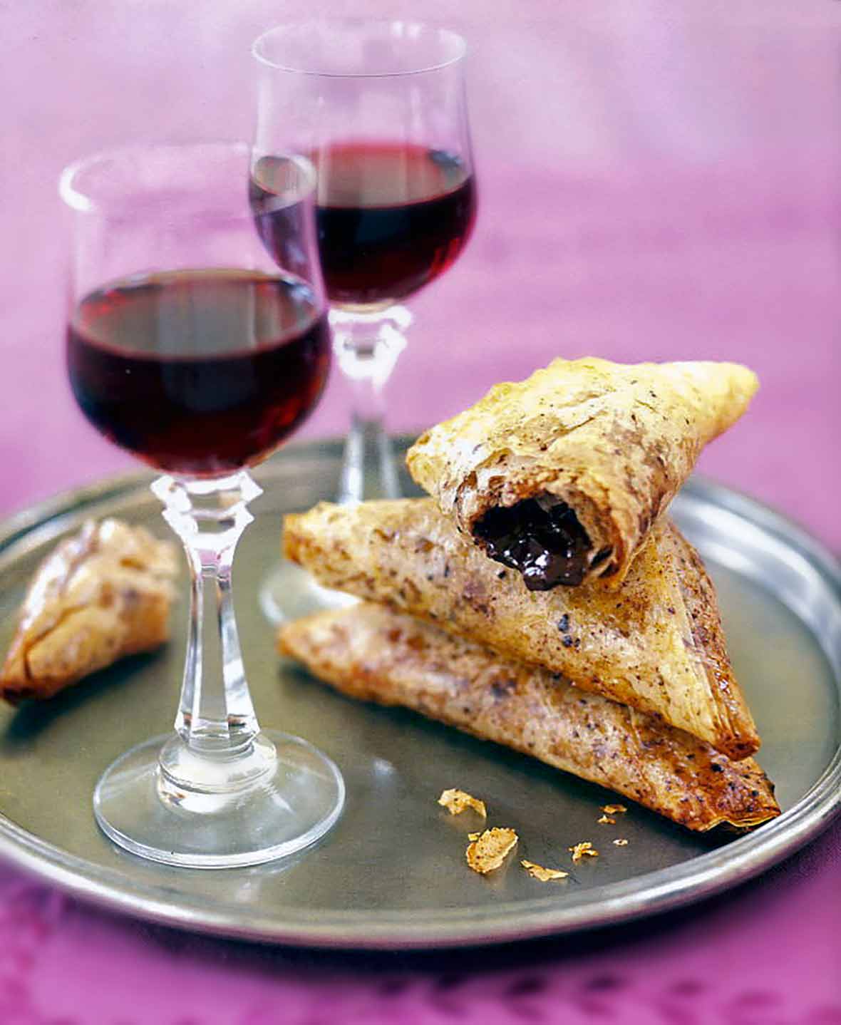 Crispy chocolate-filled pastry triangles and two glasses of dessert wine on a silver tray