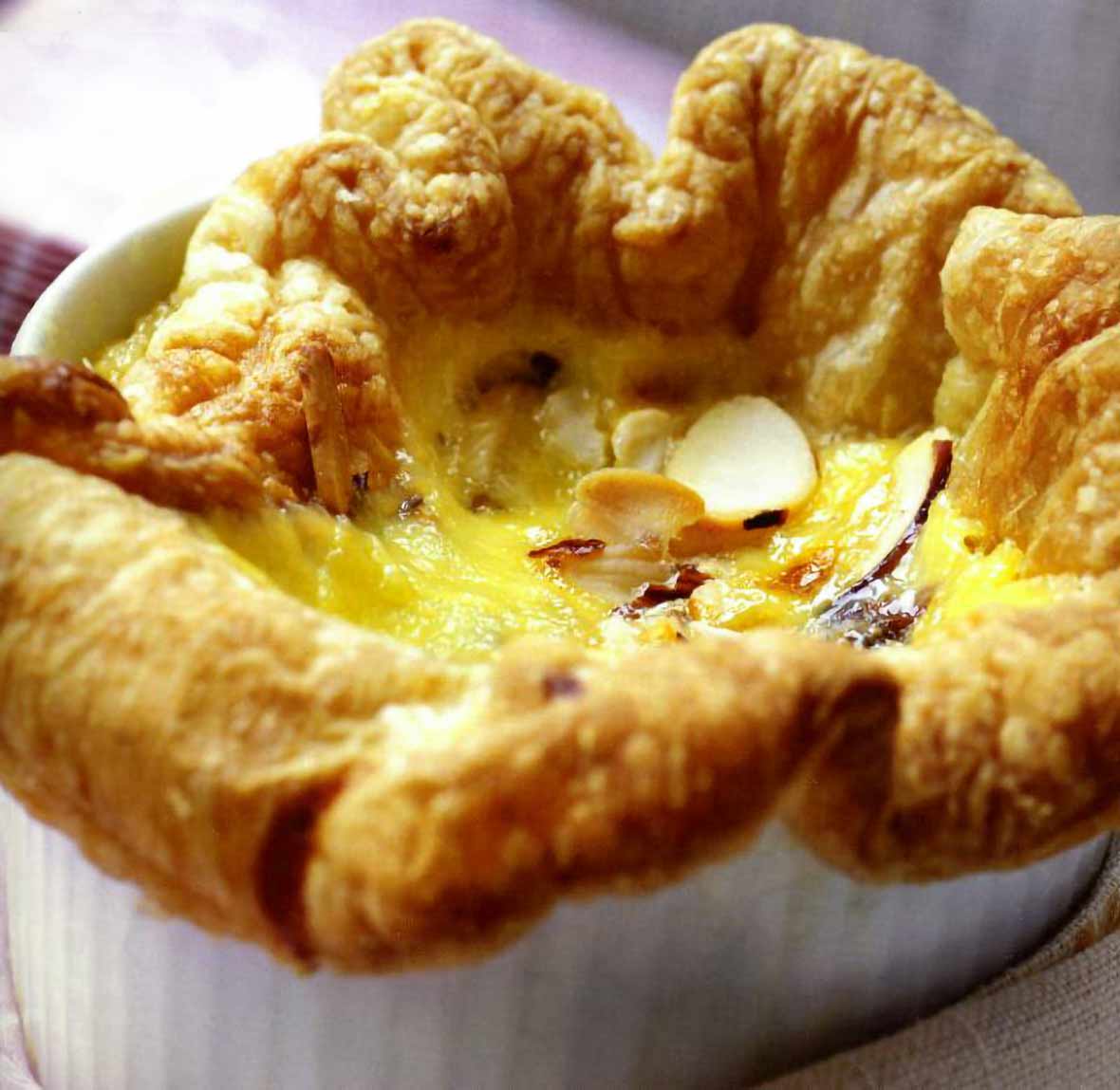 White ramekin with a baked almond custard in a pastry shell, sliced almonds on top
