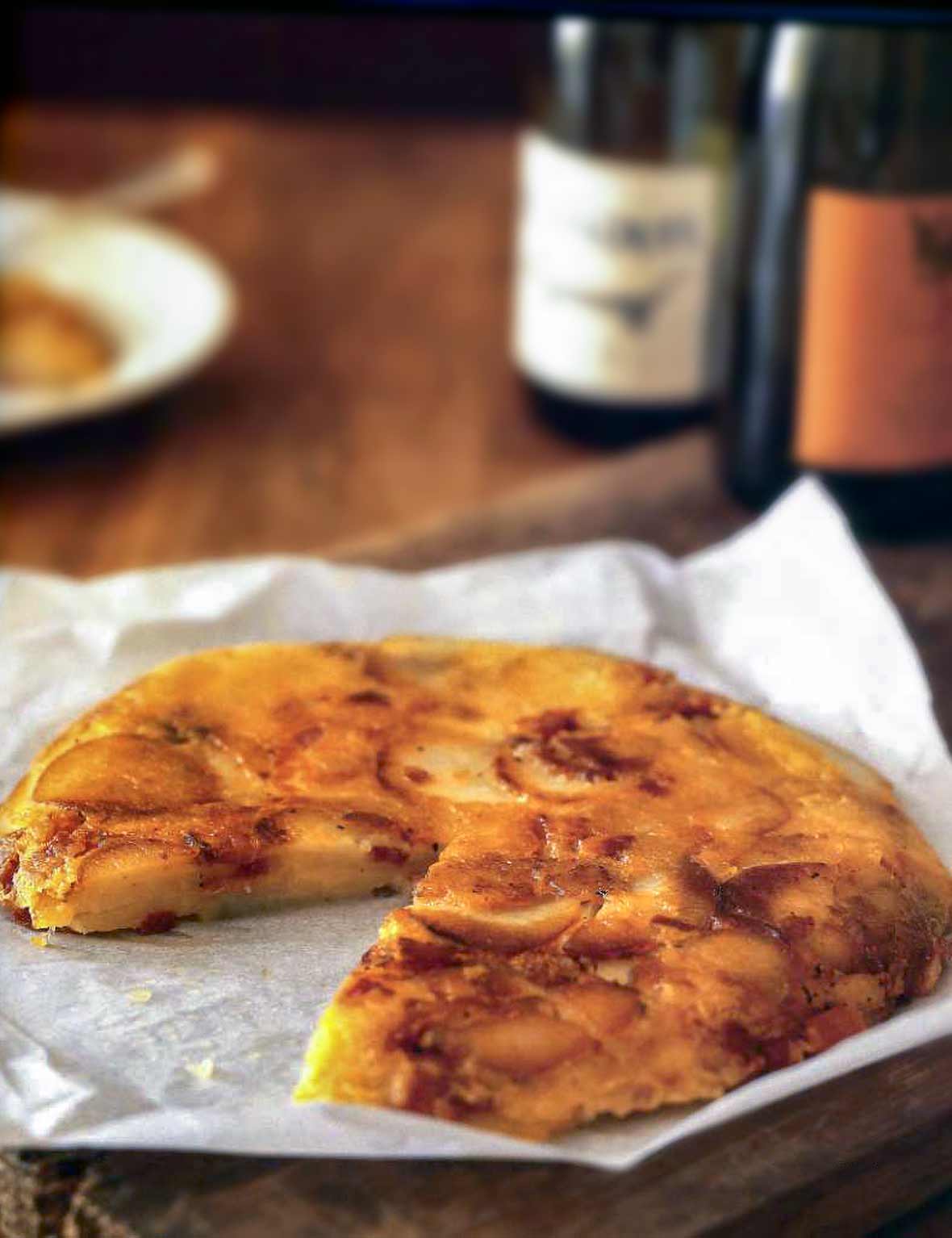 A potato pancake, with cheese and bacon, with a slice missing, on crumpled parchment