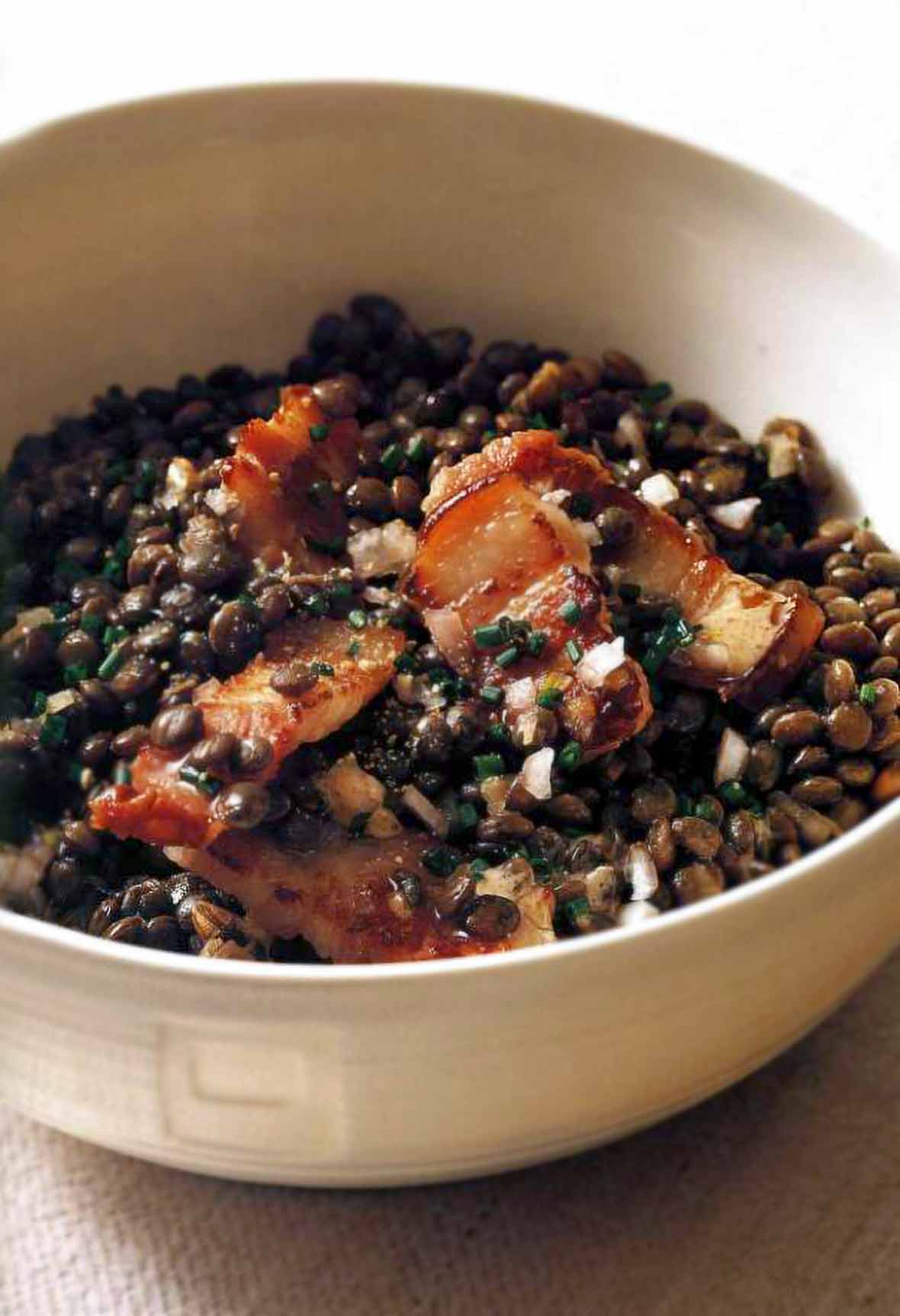 White bowl with warm lentil salad and pieces of bacon