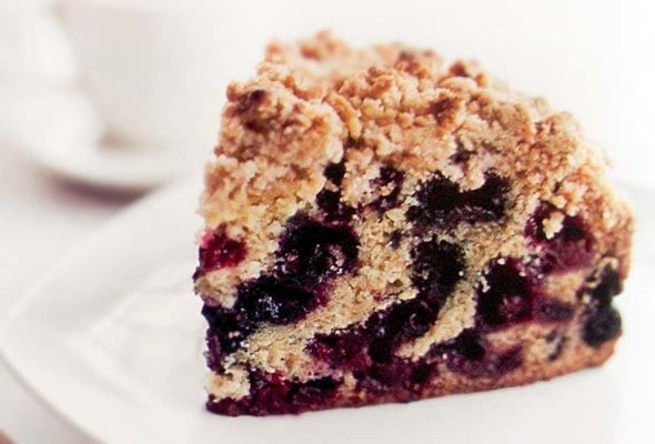 A slice of blueberry buckle with layers of blueberries and a crumb topping of butter, flour, sugar, cinnamon, and ginger