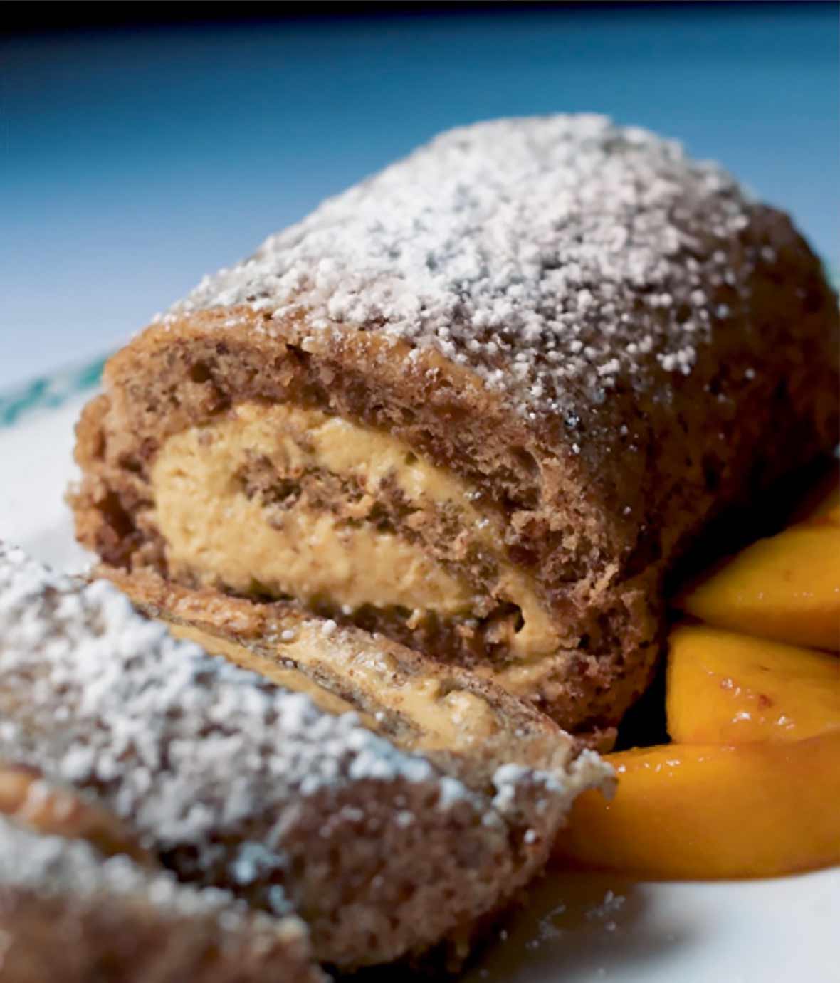 A view of the inside of a pecan roll cake with praline mousse and some peach slices on the side.