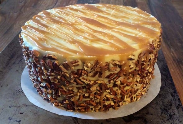 An apple spice cake with caramel sauce and a pecan crust on a parchment round.