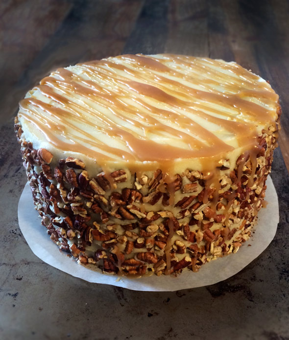 An apple spice cake with caramel sauce and a pecan crust on a parchment round.