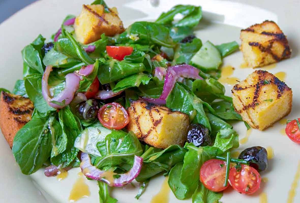 Plate of cornbread salad, grilled bread, arugula, tomatoes, onion, and herbs