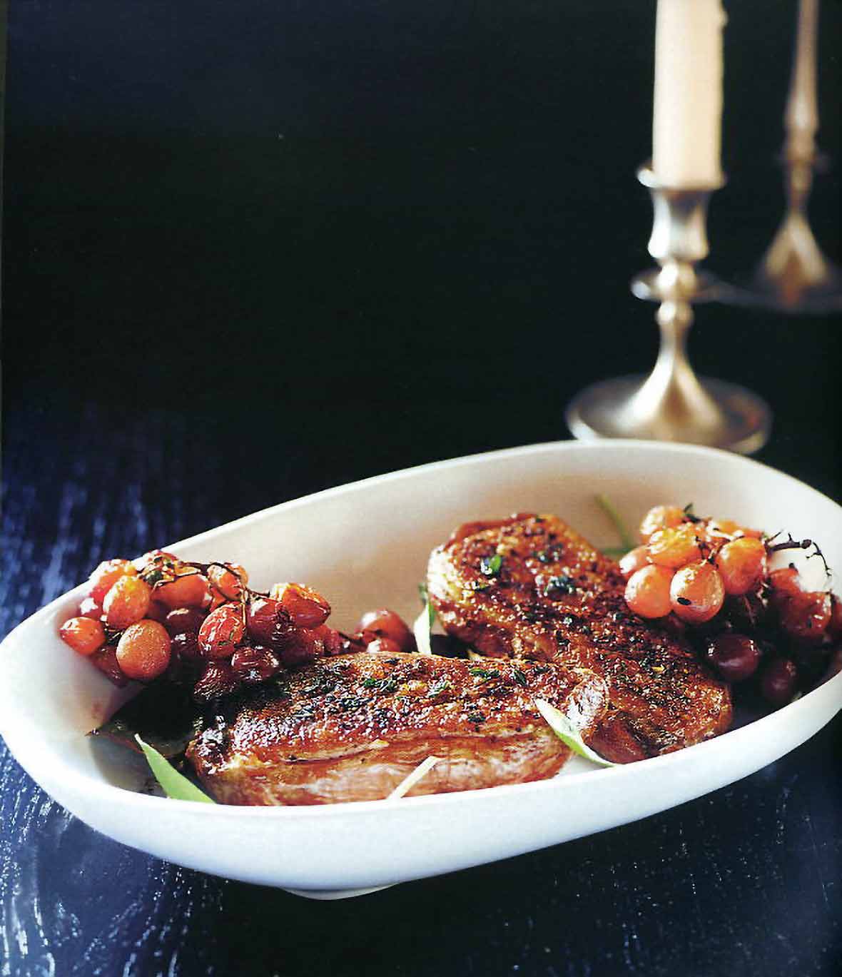 Grilled duck breasts with roasted grapes and potato-bacon gratin on a white plate on black background