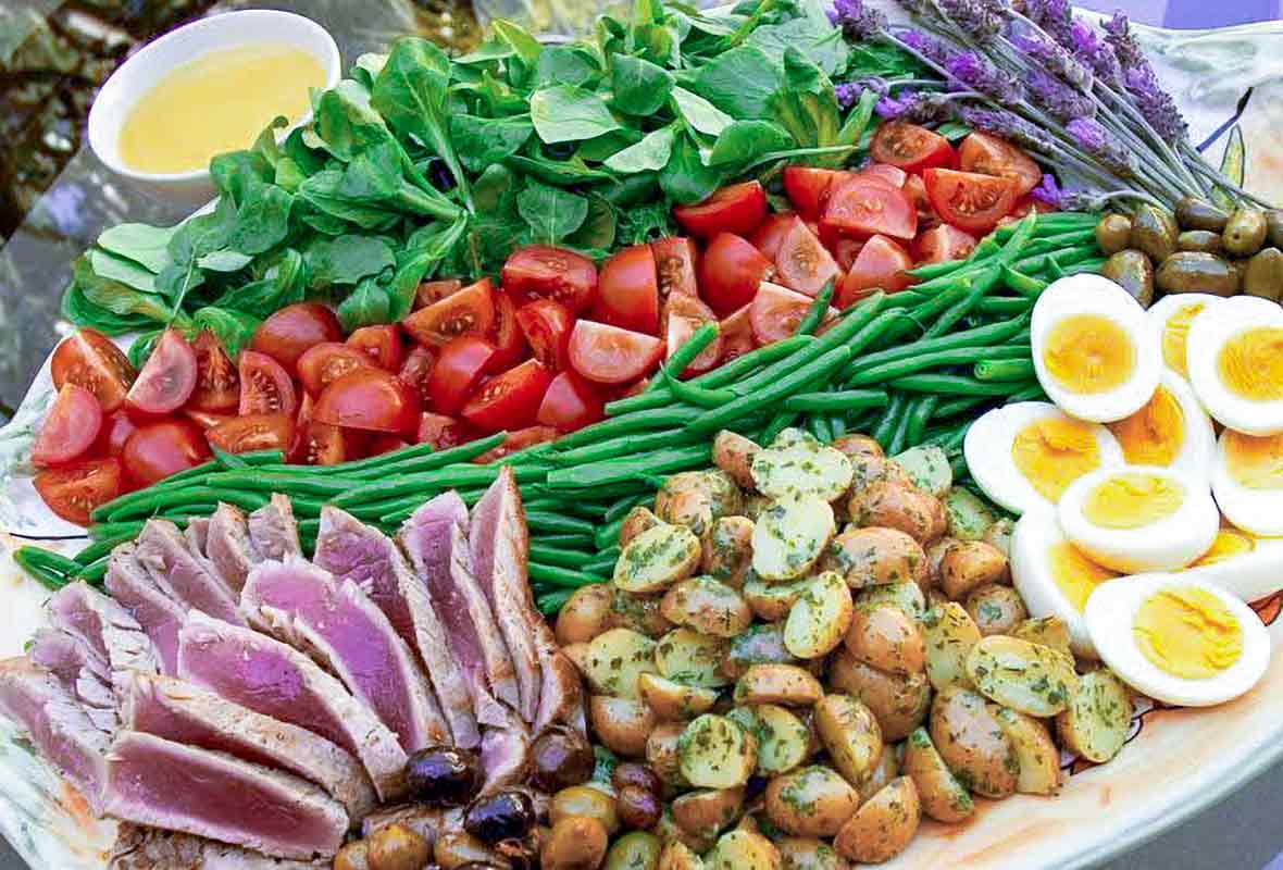 Platter of nicoise salad with slice tuna, roasted potatoes, sliced eggs, green beans, tomatoes, and greens