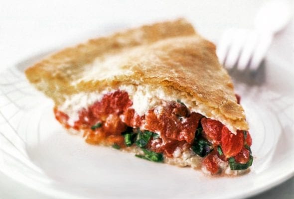 A wedge of tomato pie on a white plate with a fork in the background.
