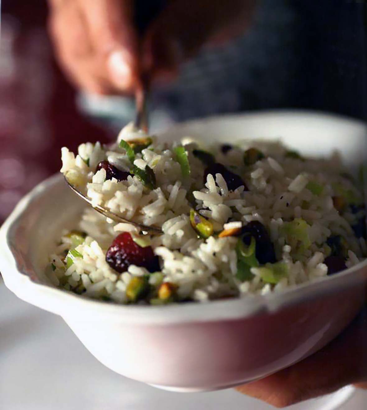 White bow of rice pilaf, dried cherries, and pistachios being stirred