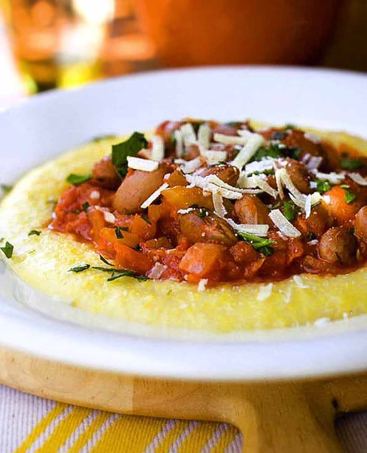 White plate of polenta topped with borlotti beans and Parnesan cheese, all on a cutting board
