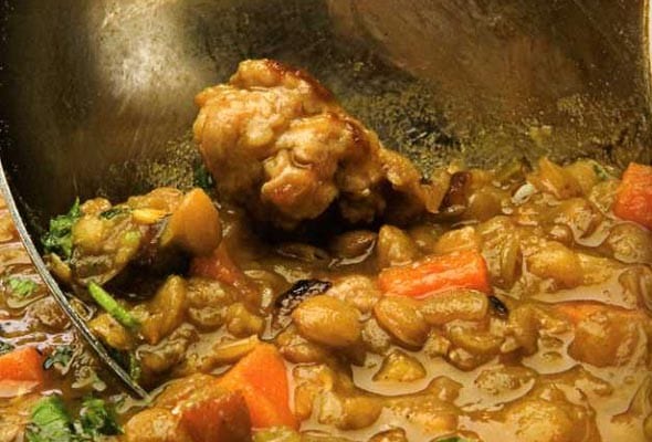 A ladle being dipped into a pot of rustic lentil soup.