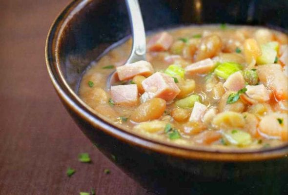 Bowl with a soup of navy beans, ham hocks, onions, celery, and parsley on brown fabric