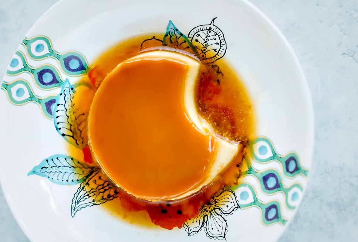 Portuguese tea flan with a caramel top and a puddle of caramel on a white plate with blue design