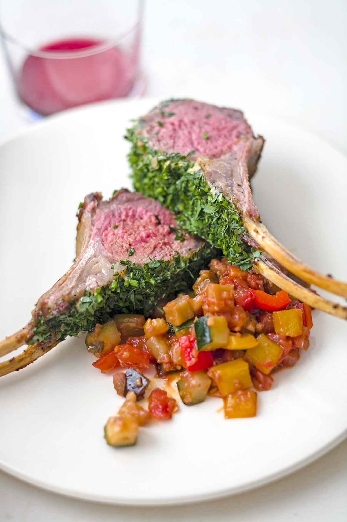 White plate with roasted rack of lamb with parsley, dijon, and chives, ratatouille nearby