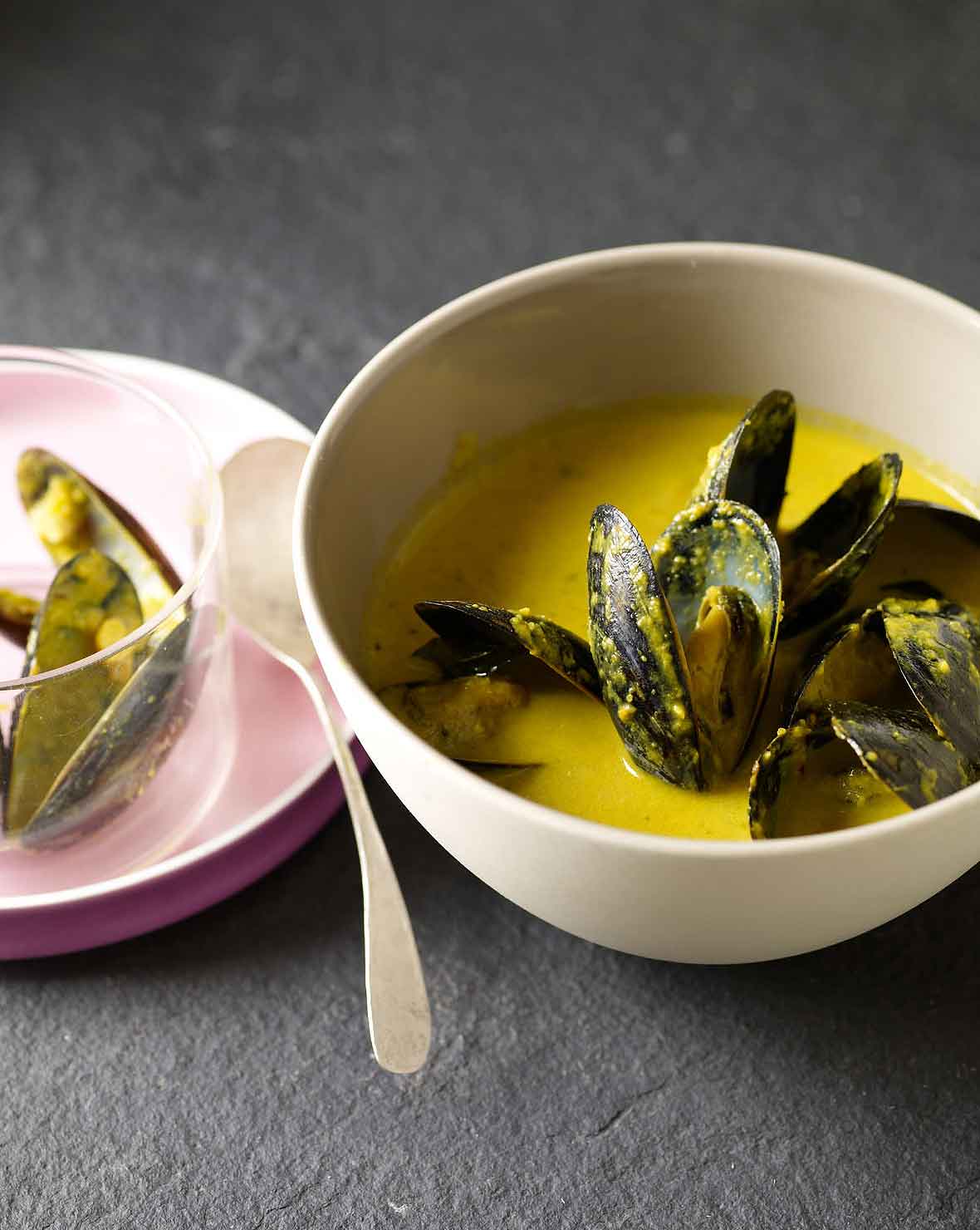 Bowl of saffron mussel stew with a yellow broth, a plate with shells to the left