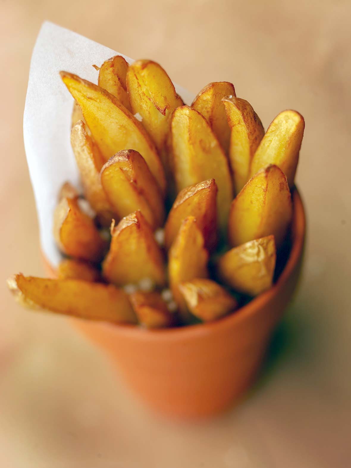 A bunch of perfect french fries in a orange cup with a piece of parchment