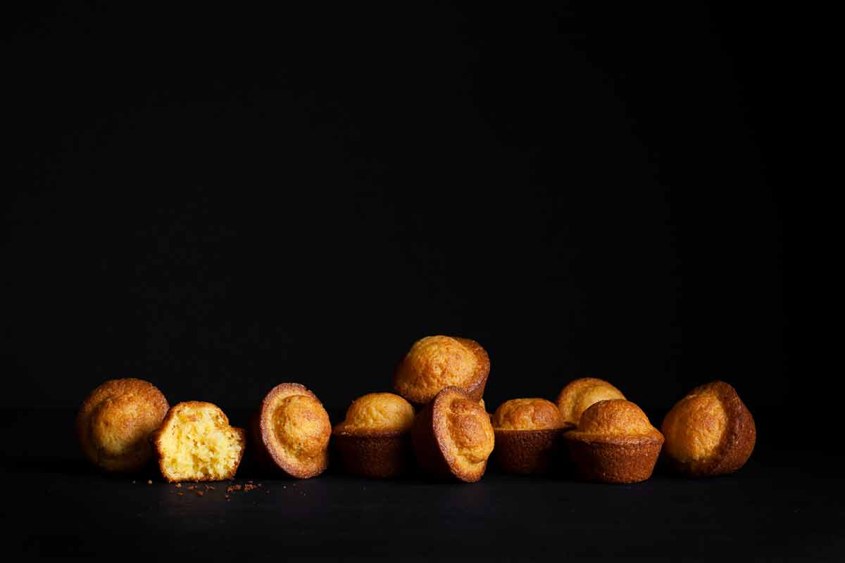 Portuguese mini lemon-orange cakes scattered on a black background with one torn in half.