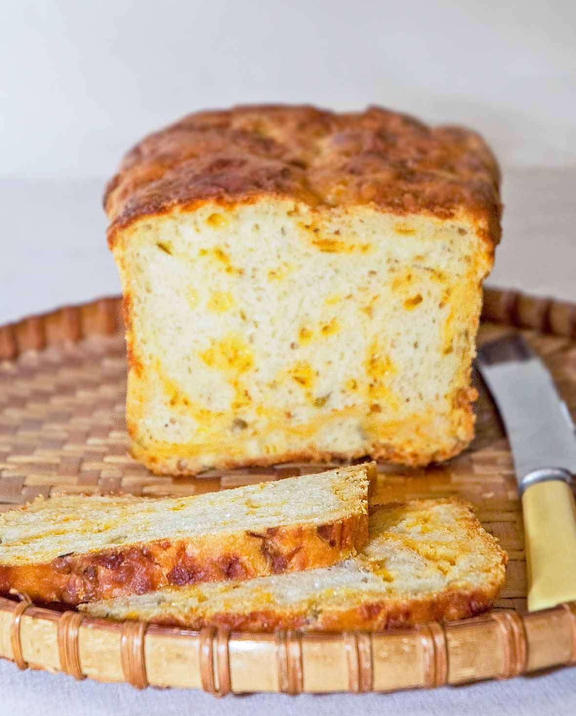 A loaf of Cheddar and chiles bread, with two slices cut, on a wicker tray