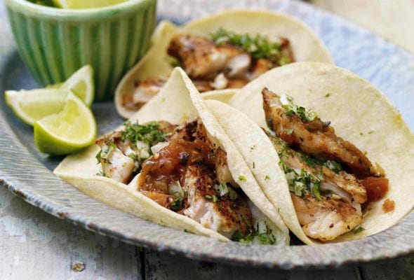 Enamel platter of three grilled red snapper tacos topped with cilantro and line, with lime wedges, beer, and chips on the side