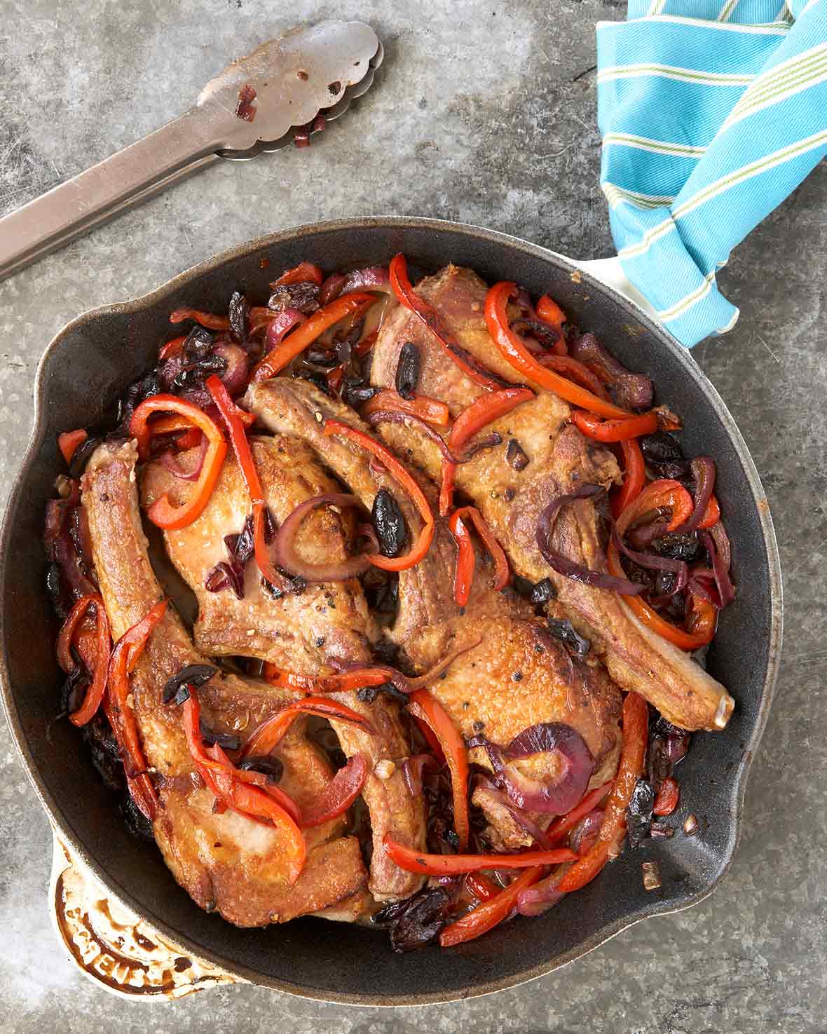 Brined pork chops cooked with red peppers, onions, black olives, and garlic in a skillet on stone