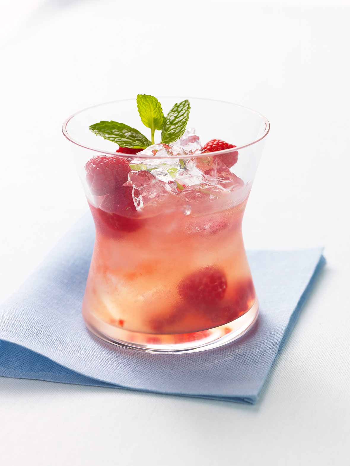Glass filled with raspberry lemonade spiked with tequila, raspberries, mint, and ice