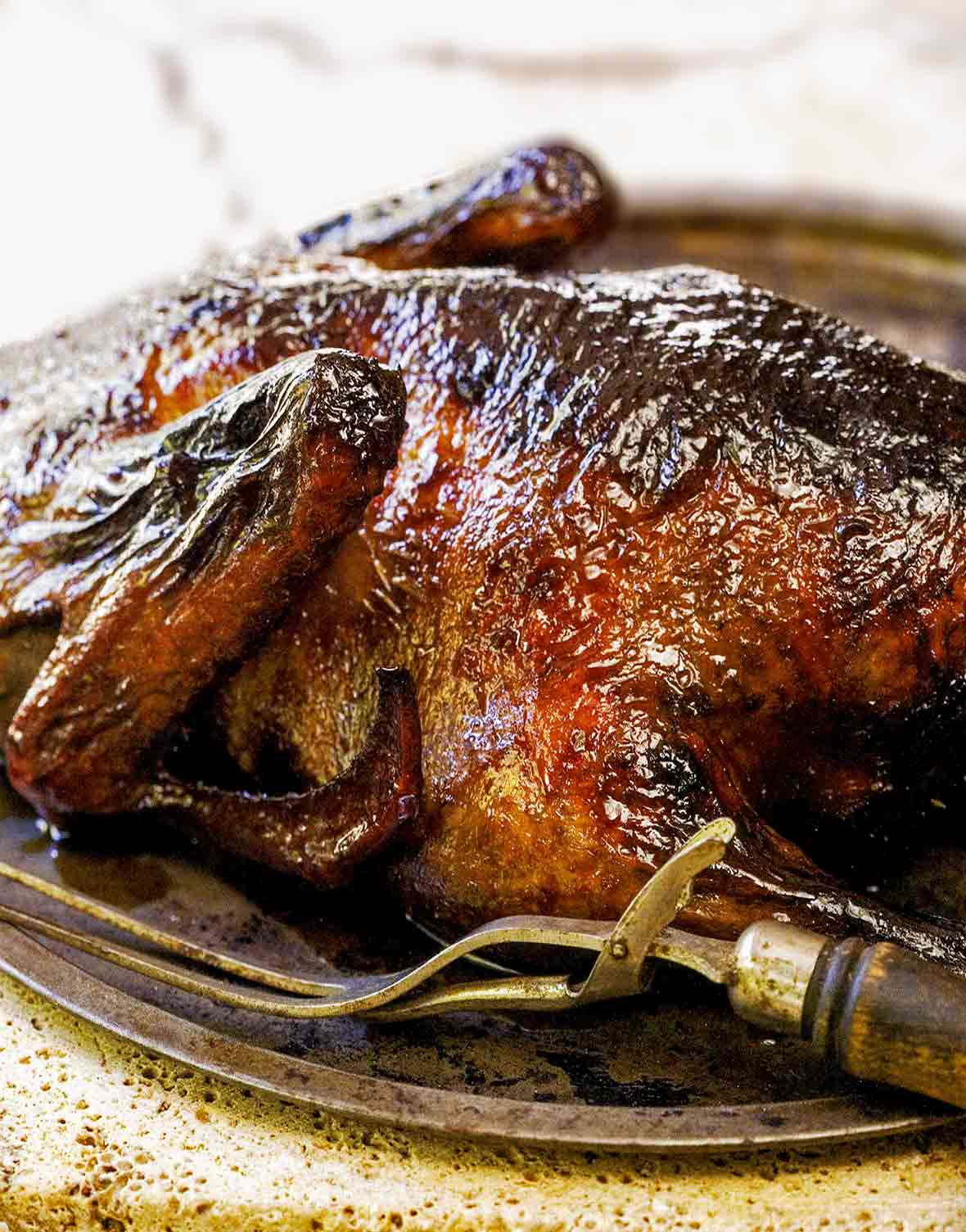Metal tray with a golden brown duck that has been tea brined., nearby is a meat fork