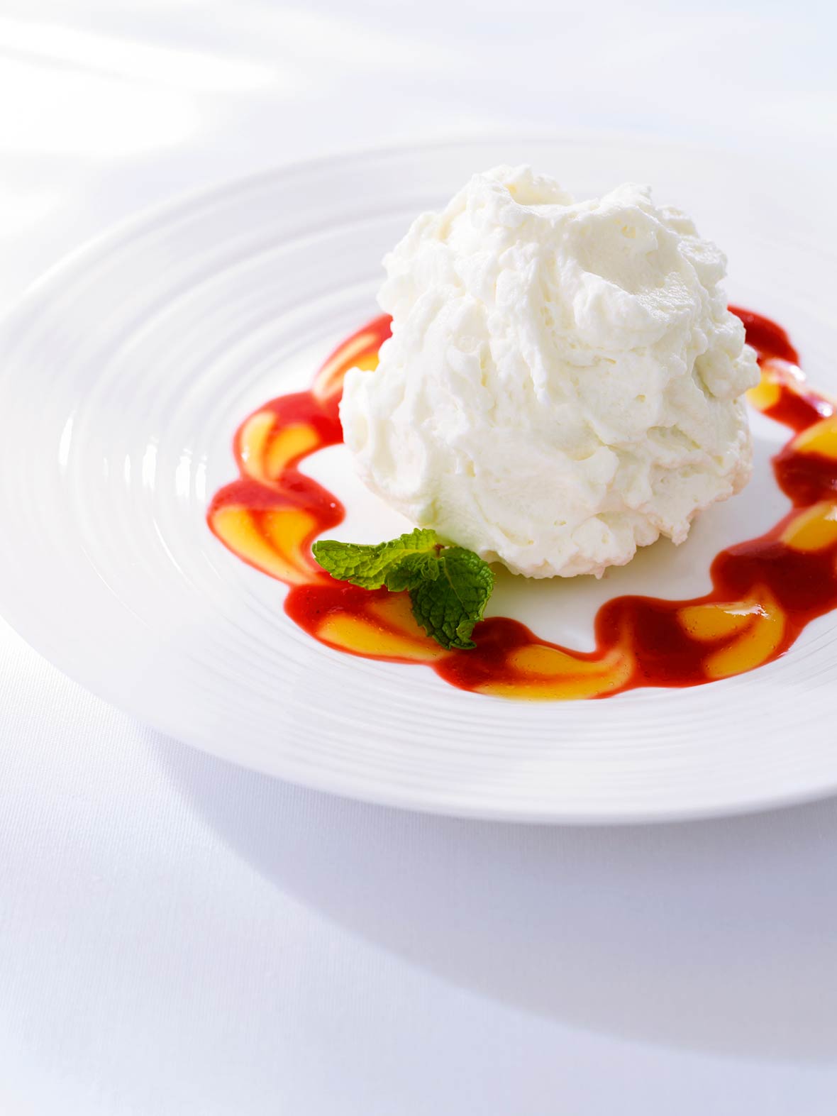 Plate of three milks cake, topped with whipped cream, with red and orange sauces