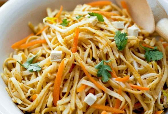 Close-up of a white bowl filled with asian noodle salad with peanut dressing, slivered carrots, tofu, and cilantro