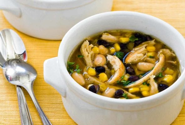 Two bowls of black and white chicken chili on a yellow placemat with two spoons beside the bowls.