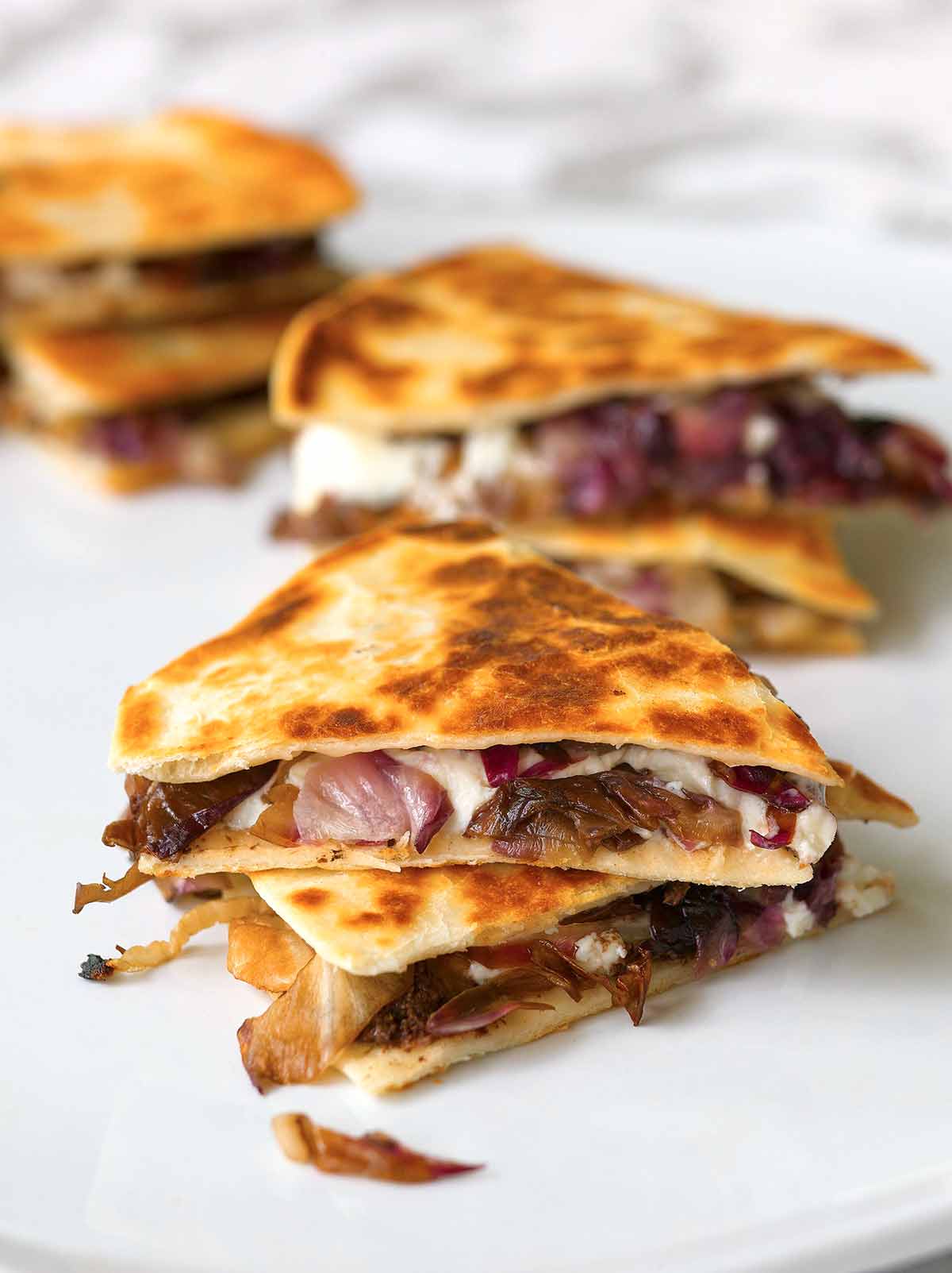 Two pieces of goat cheese quesadillas filled with radicchio, tapenade, and goat cheese stacked on top of each other.