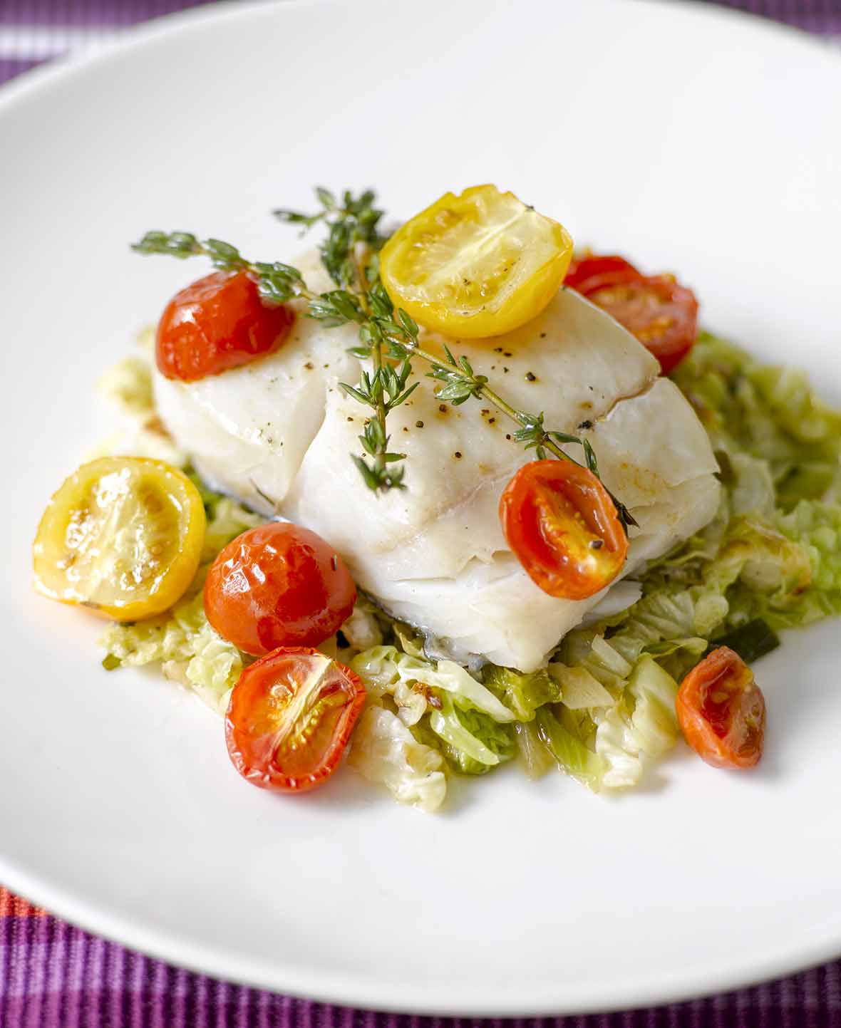 An oven-roasted halibut fillet with cherry tomatoes, and thyme on a bed of savoy cabbage