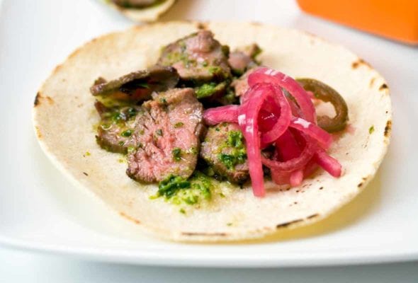 Steak tacos made of soft flour tortilla, slice steak, salsa verde, pickled onions