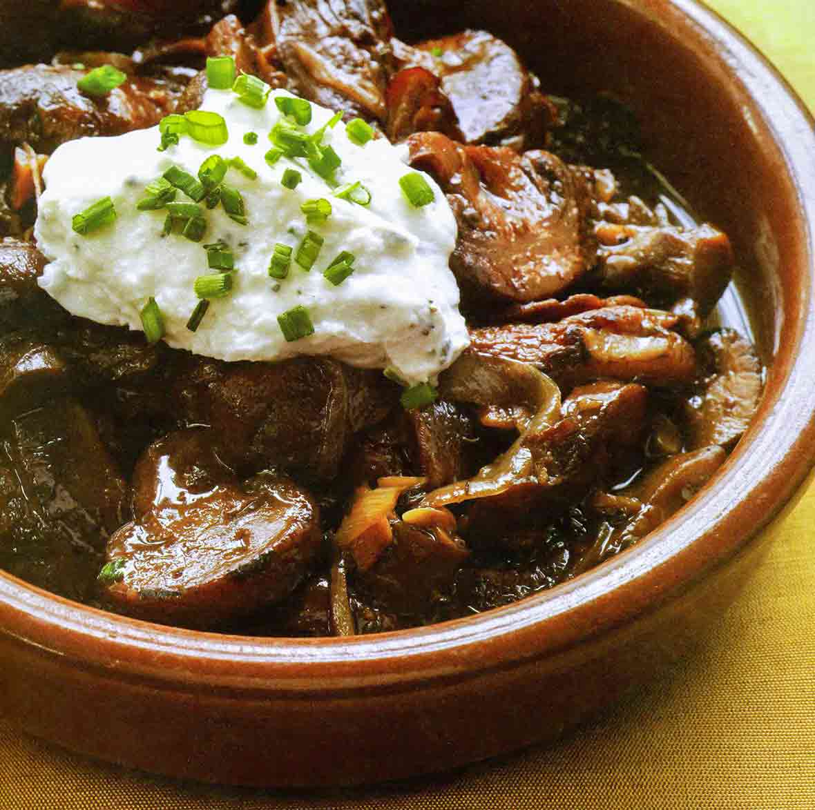 A ceramic bowl filled with wild mushrooms and herbed cheese, sprinkled with chopped chives.