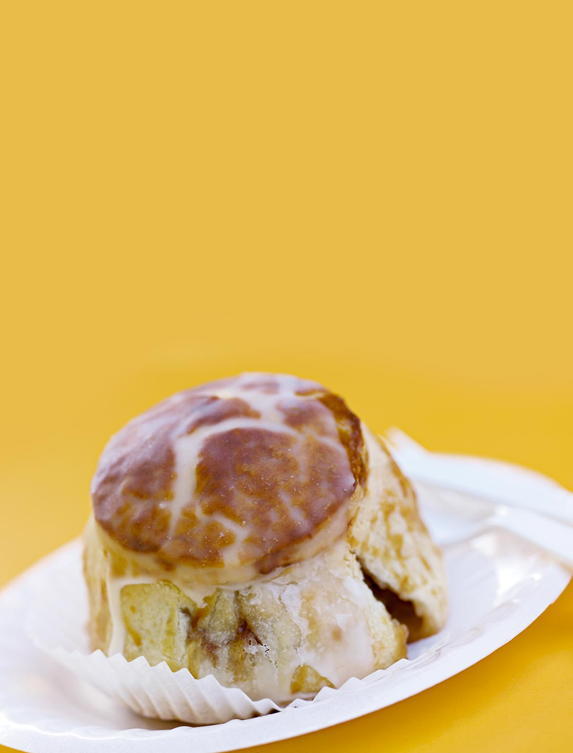 A large glazed apple dumpling on a white plate against a yellow background