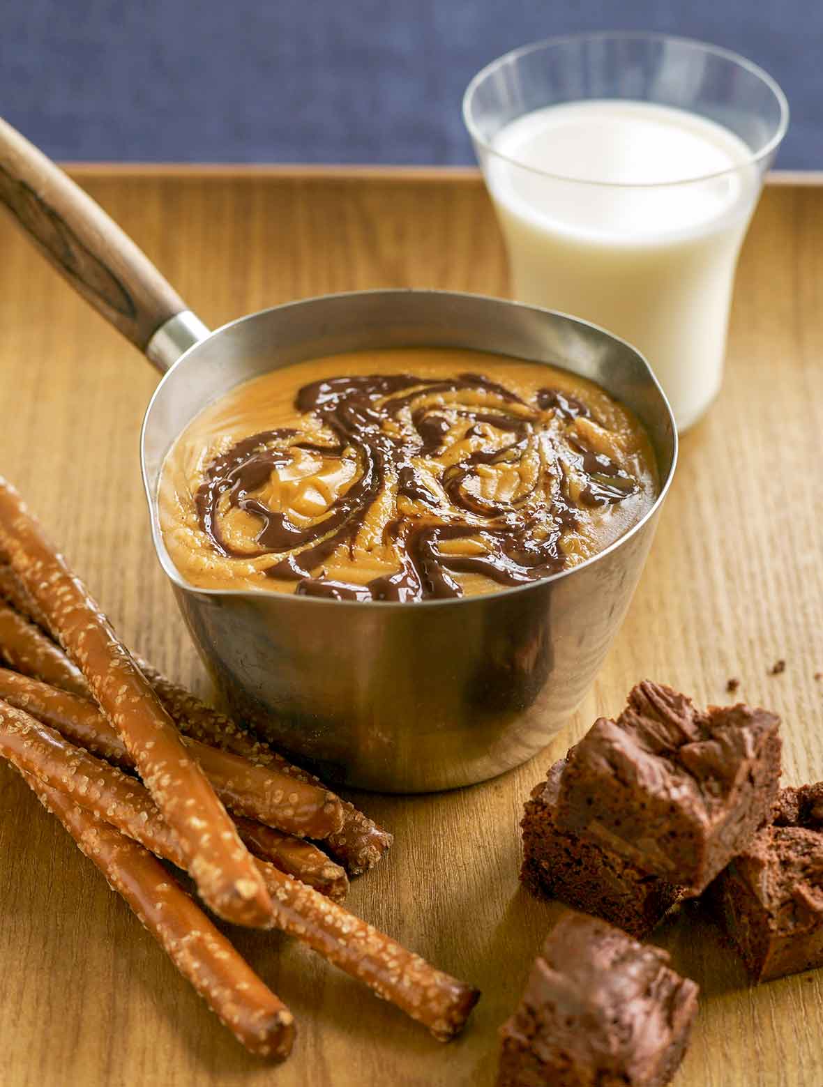 Pot of peanut butter chocolate fondue; pretzels and brownies, a glass of milk