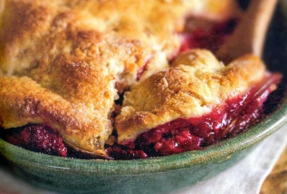 A pear and raspberry pandowdy in a green bowl with a pastry top, wooden spoon inside