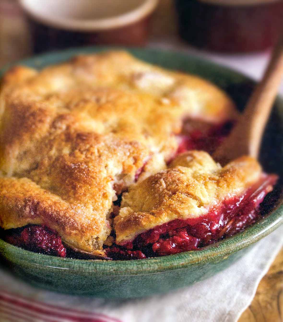 A pear and raspberry pandowdy or cobbler in a green bowl with a pastry top, wooden spoon inside