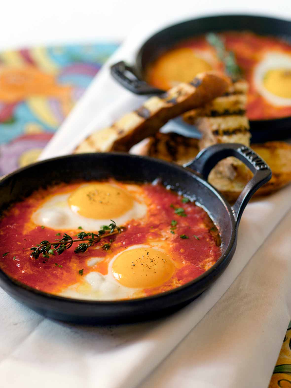 Two eggs in a tomato sauce, topped with a sprig of thyme in a cast iron skillet