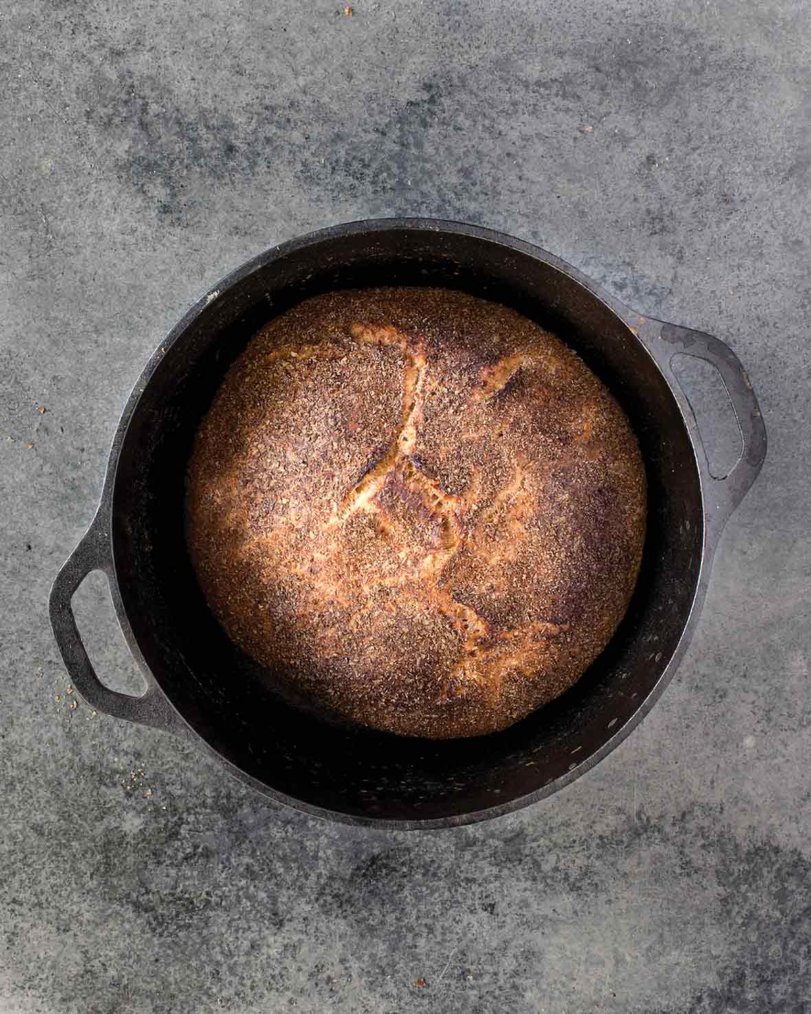 Cast-iron pot with a loaf of Jim Lahey's no-knead whole-wheat bread on a gray background