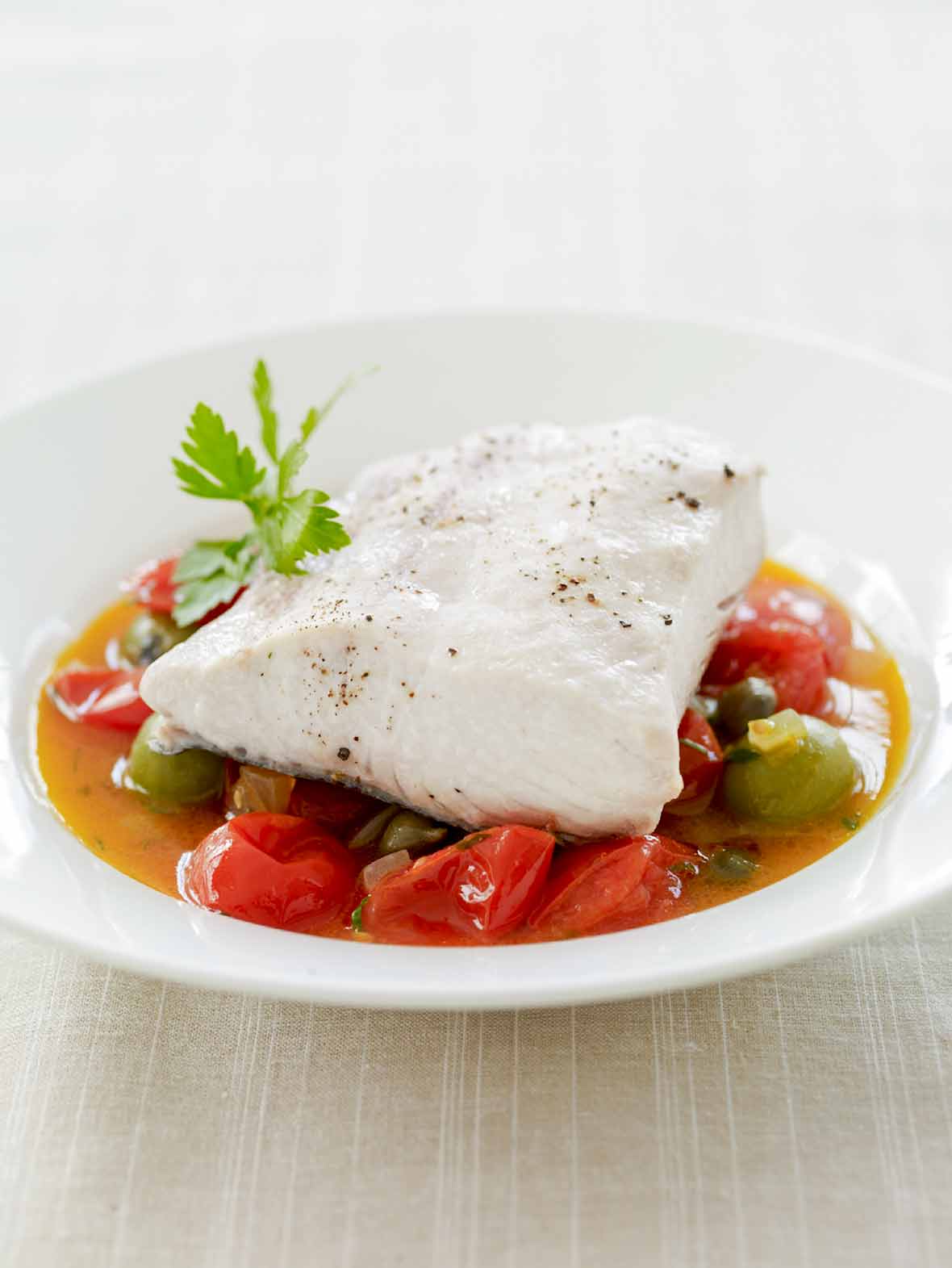 White bowl fill wth mahi mahi stewed with cherry tomatoes and capers in a broth