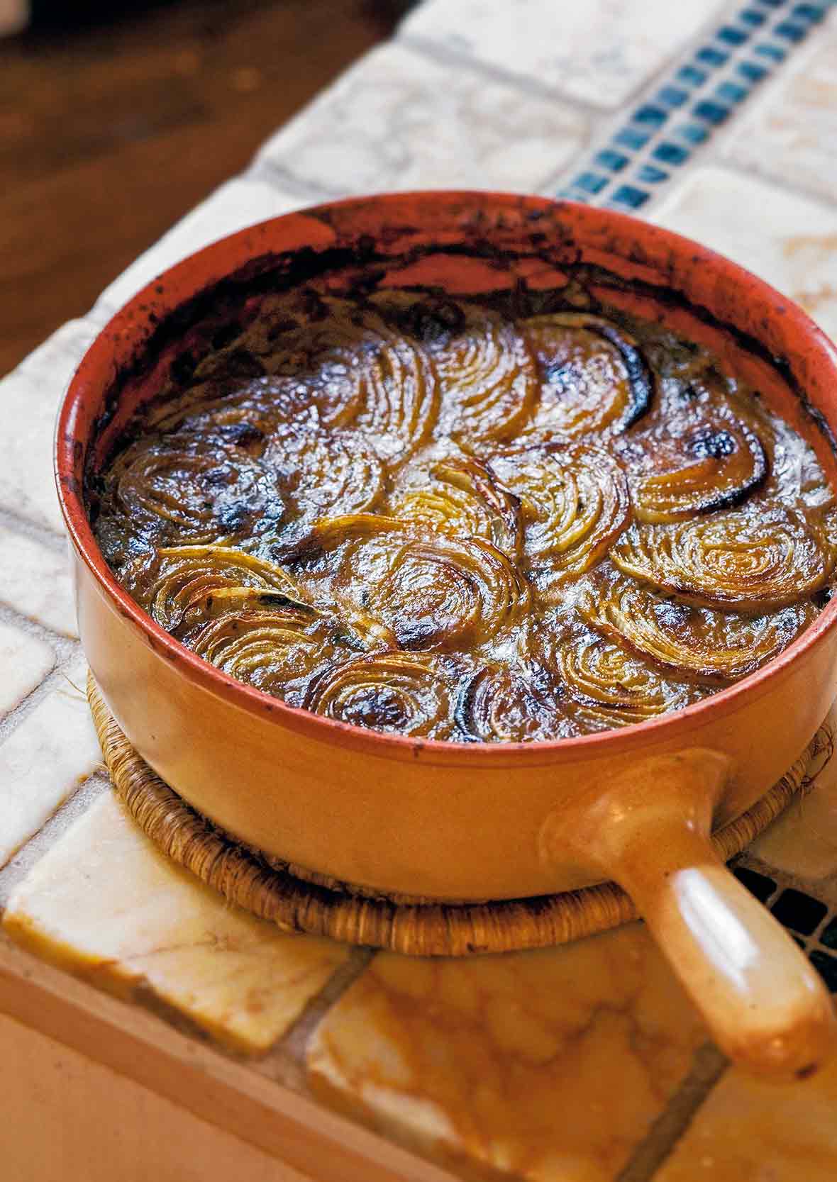 Ribollita, or Italian bread soup, in a crock topped with overlapping baked onion slices