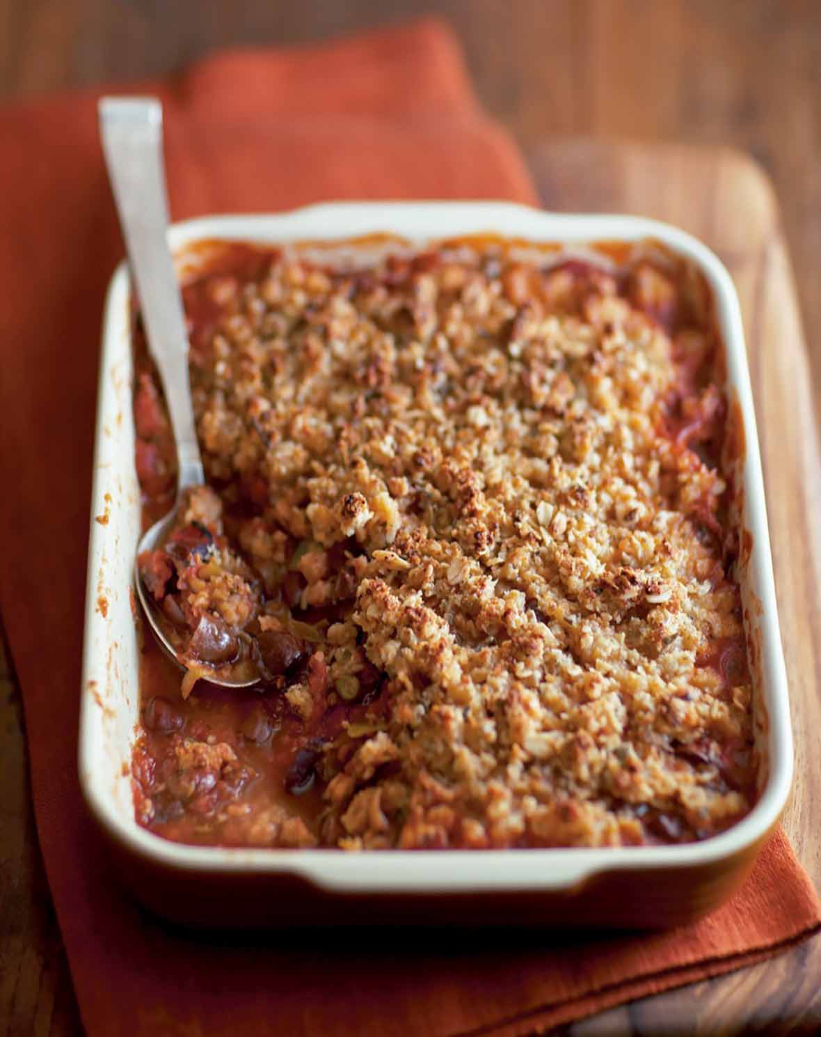 A rectangular casserole dish filled with spicy tomato crumble, and a spoon resting in it.